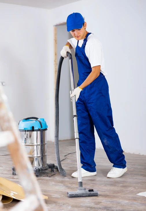 Personne utilisant une autolaveuse dans un grand entrepôt industriel avec structure métallique apparente et équipements de production en arrière-plan